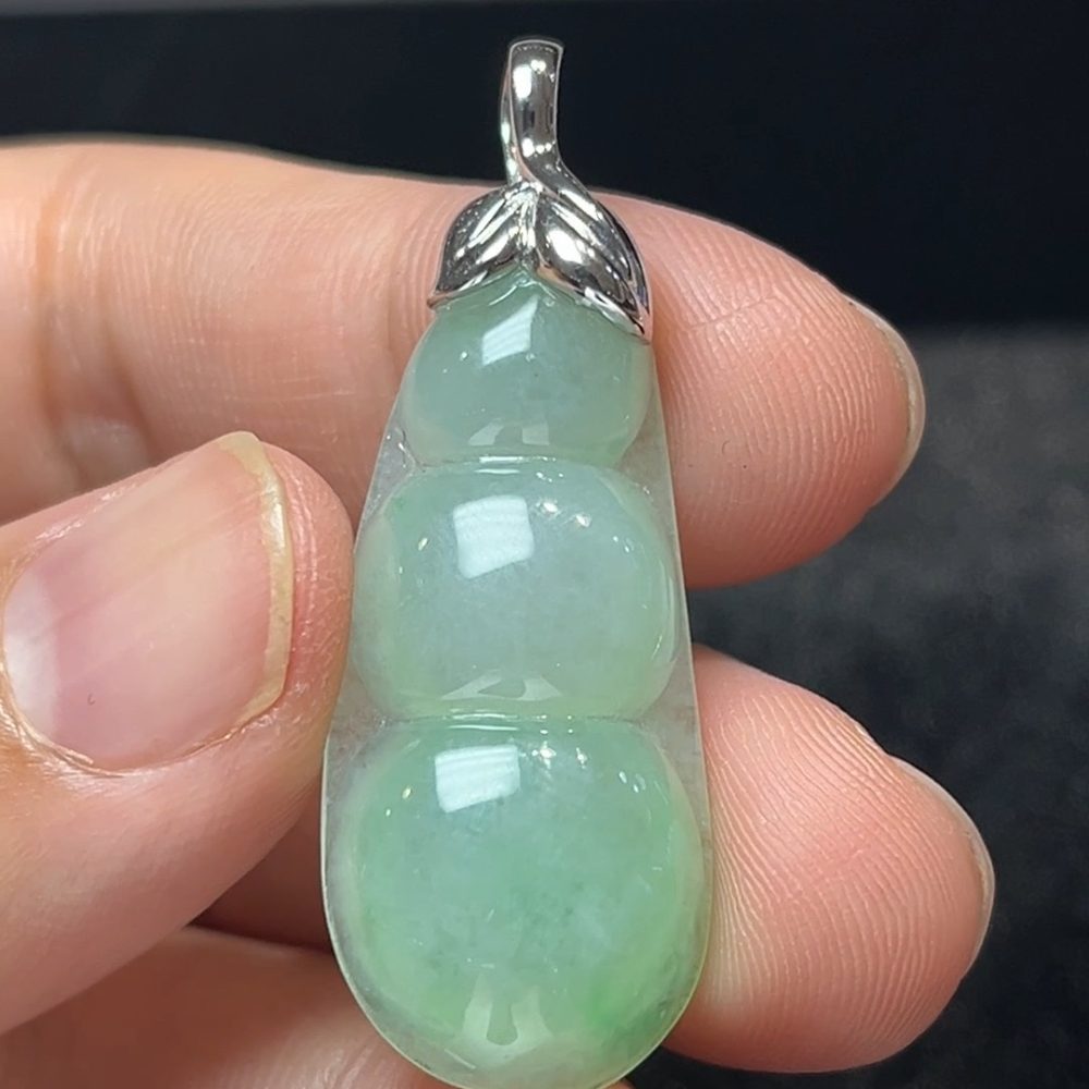 這款天然A級翡翠福豆吊墜（編號#275），採用質地溫潤通透的淺綠翡翠雕琢而成，外型為傳統「福豆」造型，線條飽滿圓潤，寓意多福多壽、子孫綿延。吊墜頂部搭配18K白金鑲嵌莖部設計，如嫩芽破土，點出生命力與新生之意，同時提升整體工藝質感與佩戴穩定性。融合東方寓意與現代簡約感，是一件兼具文化與時尚氣息的雅緻吊墜。
